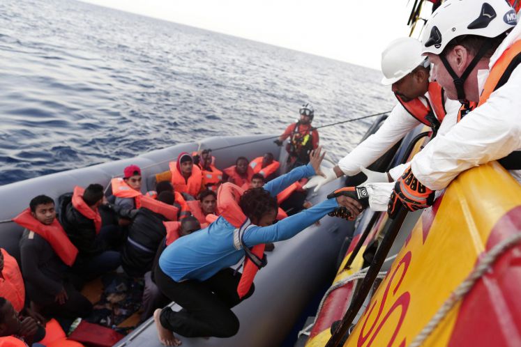 Mitglieder des italienischen Roten Kreuzes retten afrikanische Flüchtlinge aus einem Schlauchboot im Mittelmeer