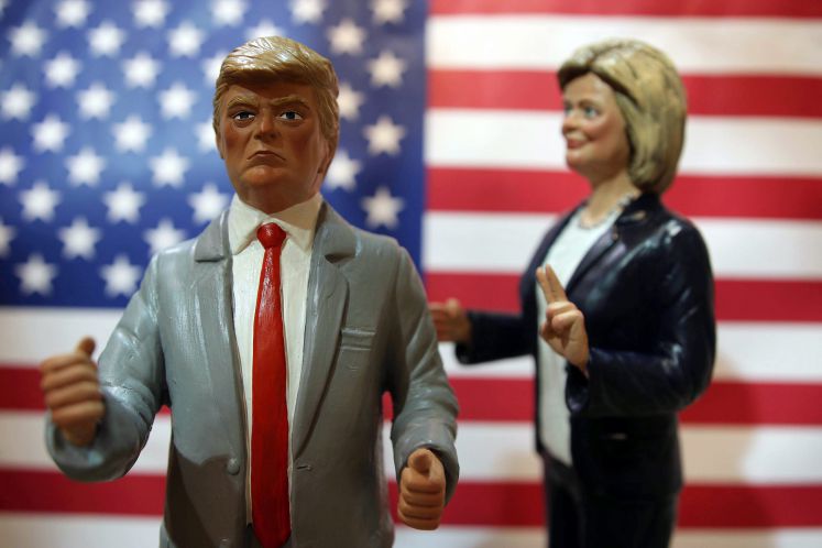 Trump und Clinton als Figuren abgebildet. Er im Vordergrund mit geballten Fäusten, sie im Hintergrund mit der Victory-Geste.