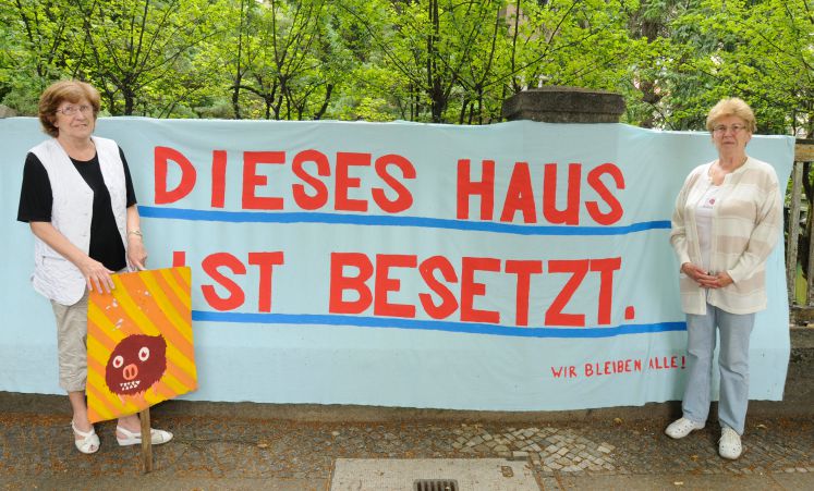 Die Rentnerinnen Brigitte Gall (r) und Ursula Pinotek stehen vor dem besetzten Seniorenklub in Berlin-Pankow, zwischen ihnen hängt ein Banner mit der Aufschrift "Dieses Haus ist besetzt. Wir bleiben alle!".