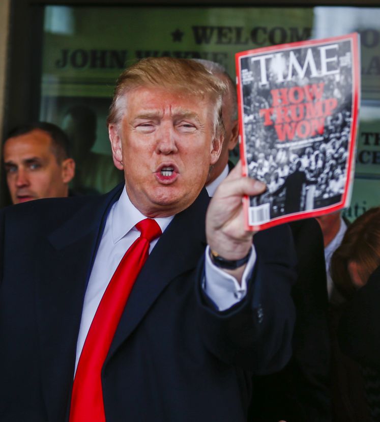 Donald Trump hält eine Ausgabe des Magazins Time in der Hand, auf dem steht "How Trump won" - wie Trump gewonnen hat