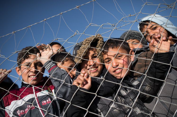 Flüchtlingskinder schauen durch einen Maschendrahtzaun