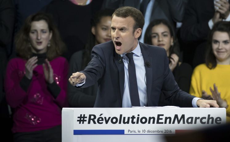 Emmanuel Macron während einer Rede mit ausgestreckter Hand und Zeigefinger spricht her hinter dem Pult "#RévolutionEnMarche"