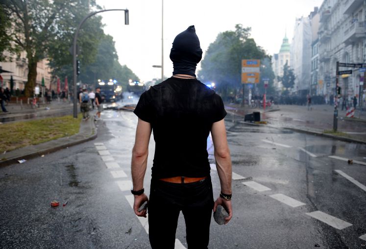 Ein Aktivist steht mit dem Rücken zur Kamera und Steinen in beiden Händen.