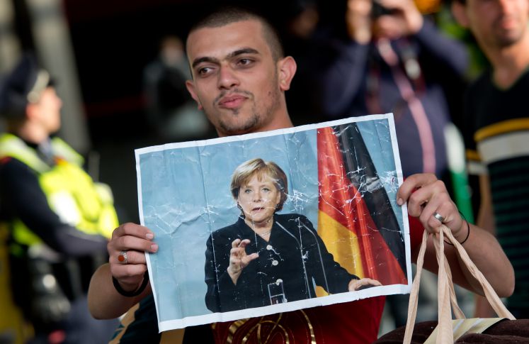 Ein Flüchtling, der kurz zuvor mit einem Zug angekommen ist, läuft am 05.09.2015 auf dem Hauptbahnhof in München (Bayern) über den Bahnsteig und hält dabei ein Foto von Angela Merkel in den Händen. 