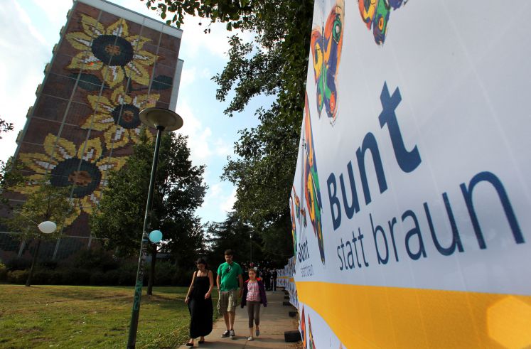Passanten gehen im Rostocker Stadtteil Lichtenhagen neben dem Sonnenblumenhaus an Transparenten der Initiative «Bunt statt braun» vorbei.