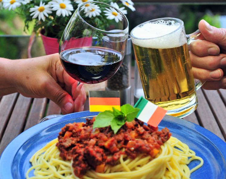 Mit italienischem Rotwein und deutschem Bier stoßen ein Mann und eine Frau am 26.06.2012 auf einem Balkon in Chemnitz an. Im Vordergrund ist ein Teller Spaghetti, geschmückt mit einer deutschen und einer italienischen Flagge zu erkennen. 