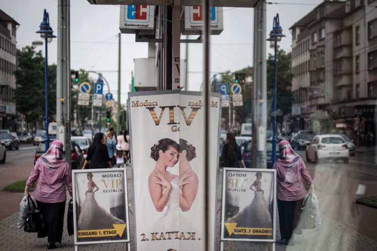 Eine Frau mit Kopftuch geht in Duisburg-Marxloh neben einem Geschäft mit Hochzeitsbekleidung vorbei.