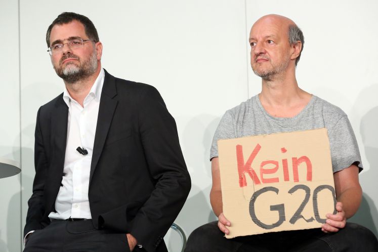 Ein Teilnehmer (r) einer Infoveranstaltung zum G20-Gipfel in Hamburg (07.-08.07.2017) sowie OSZE-Gipfel (08.-09.12.2016) protestiert am 01.09.2016 in Hamburg auf dem Podium mit einem Pappschild mit der Aufschrift «Kein G20». Neben ihm steht der Staatsrat der Senatskanzlei, Wolfgang Schmidt (l).