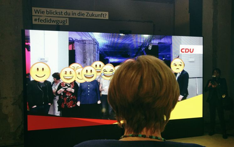 Merkel steht vor der Emoji-Wand im fedidwgugl-Haus in Berlin Mitte.
