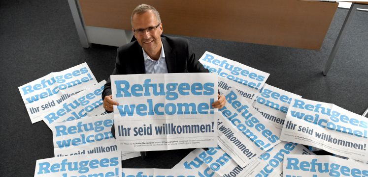 Der Chefredakteur der Kieler Nachrichten inmitten von Schildern mit der Aufschrift "Refugees welcome"