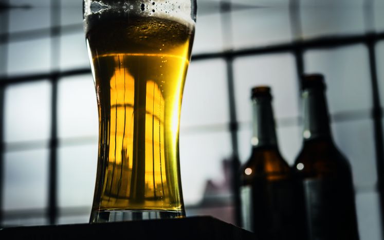 Nahaufnahme eines Glases Bier, im Hintergrund zwei Bierflaschen
