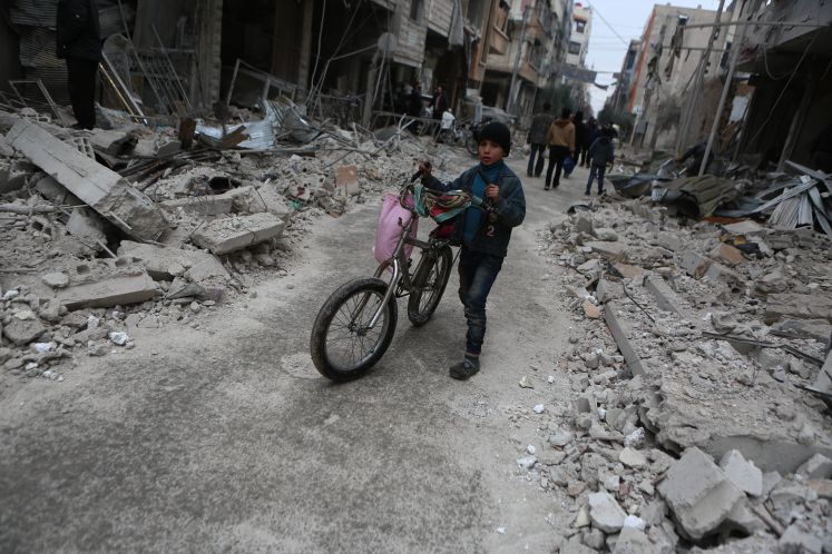 Ein kleiner Junge schiebt umgeben von Trümmern und Häuserskeltten sein Fahrrad.