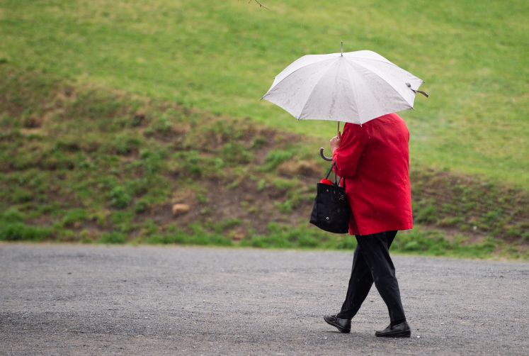 Eine Frau mit Regenschirm und rotem Mantel geht am Potsdamer Platz durch den Regen