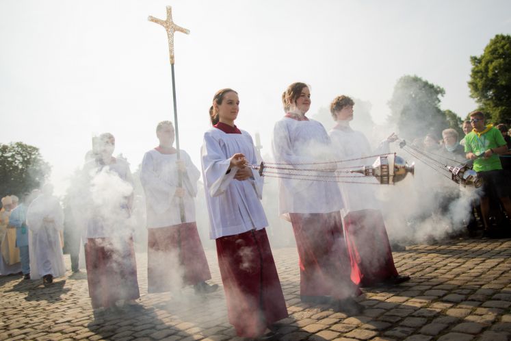 Katholiken bei einer Prozession mit goldenem Kreuz und Weihrauch.