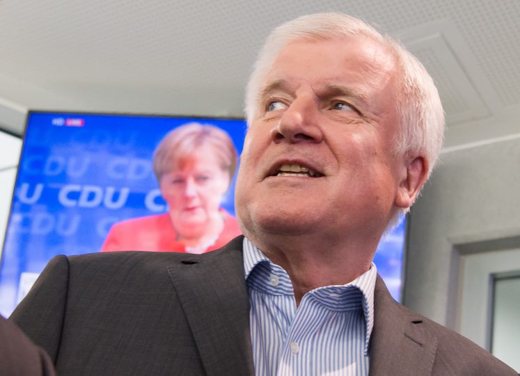 Horst Seehofer, CSU-Vorsitzender und Bundesminister für Inneres, Heimat und Bau, läuft auf seinem Weg zu einer Pressekonferenz, die in Anschluss an die Sitzung des CSU-Vorstands stattfindet, an einem Fernseher vorbei, auf dem die Pressekonferenz von Bundeskanzlerin Angela Merkel übertragen wird. 