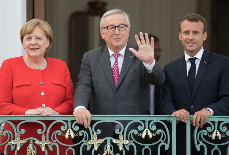 Emmanuel Macron (r), Präsident von Frankreich, Jean-Claude Juncker (M), Präsident der Europäischen Kommission, und Angela Merkel (CDU), Bundeskanzlerin, unterhalten sich zum Deutsch-Französischen Ministerrat vor Schloss Meseberg