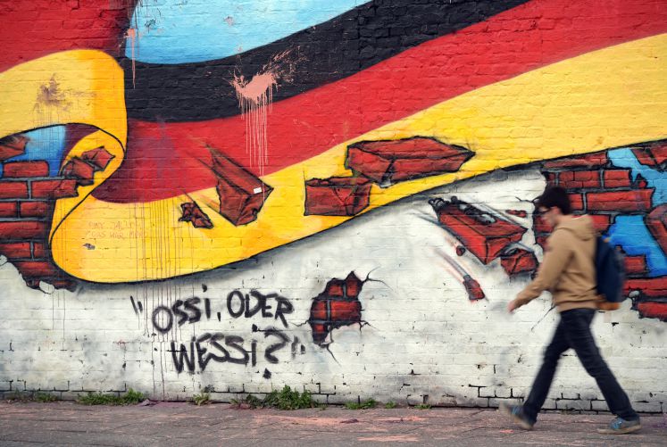 Ein Passant geht in Berlin an an einem Wandbild mit der deutschen Nationalflagge und dem Schriftzug "Ossi oder Wessi? vorbei. 