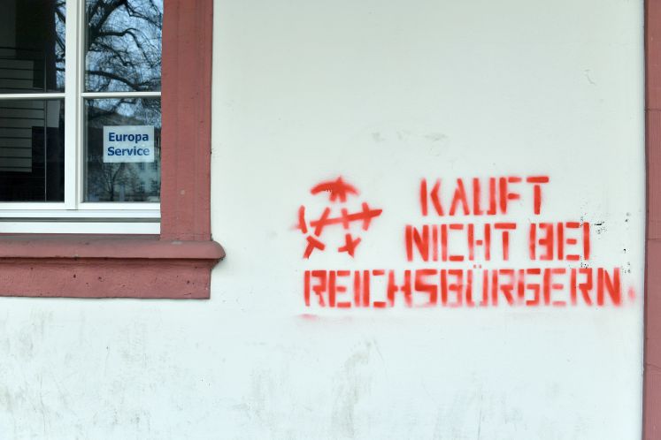 Mit roter Farbe ist der Spruch "Kauft nicht bei Reichsbürgern" und ein vermutliches Antifa-Symbol an eine Hauswand in Erfurt (Thüringen) gesprüht worden