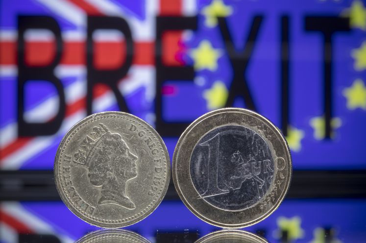 Eine Euro- und eine Pound-Münze stehen voreinander. Im Hintergrund steht Brexit geschrieben vor der europäischen und britischen Flagge.