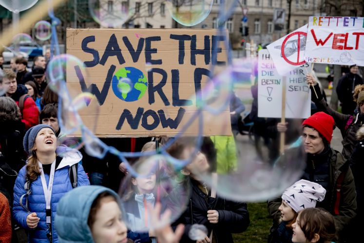 22.03.2019, Berlin: Seifenblasen schweben vor einem Plakat mit der Aufschrift „Save the World Now", das jugendliche Teilnehmer der Klima-Kundgebung "Friday for Future" am Invalidenpark halten.