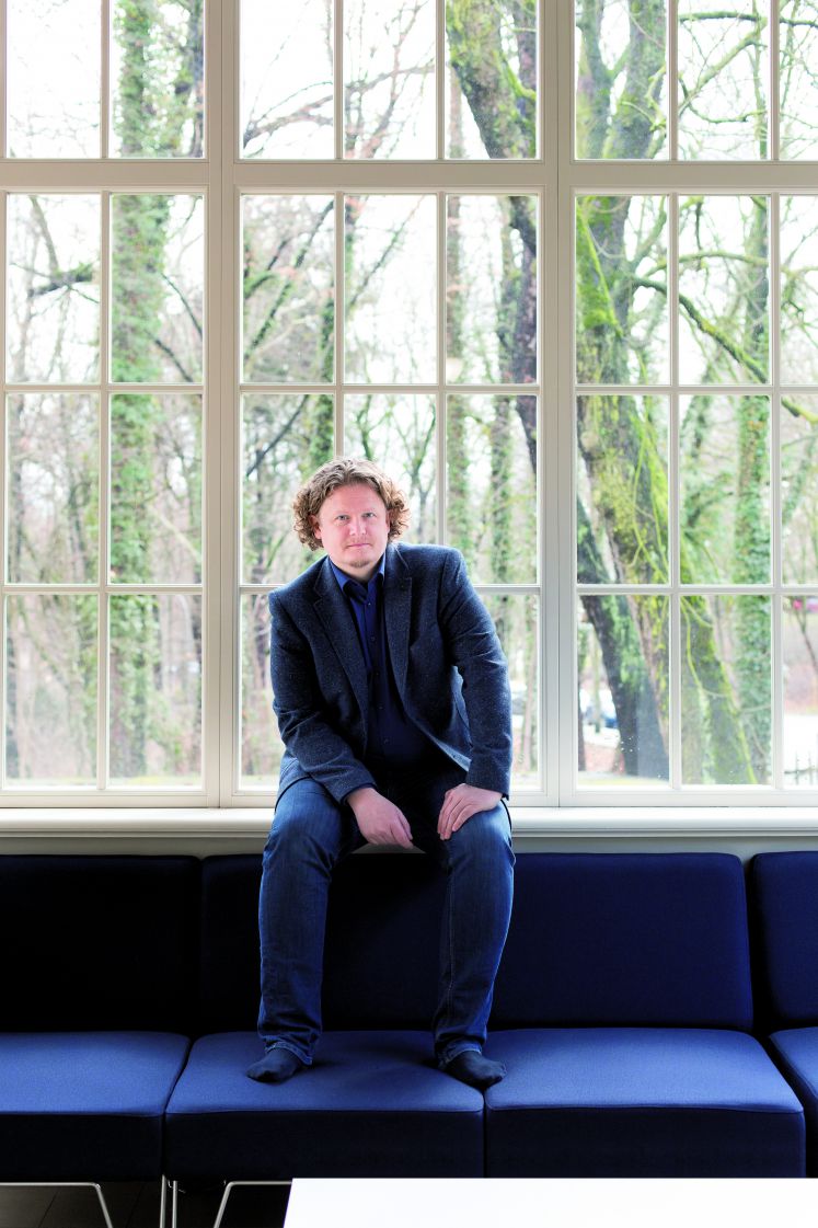 Lars Fassmann sitzt auf einer Fensterbank, die Füße auf einem Sofa abgestellt