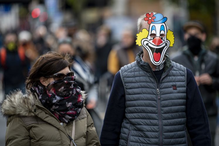 Mann mit Clownsmaske und Frau mit Schal vor dem Gesicht in Fußgängerzone
