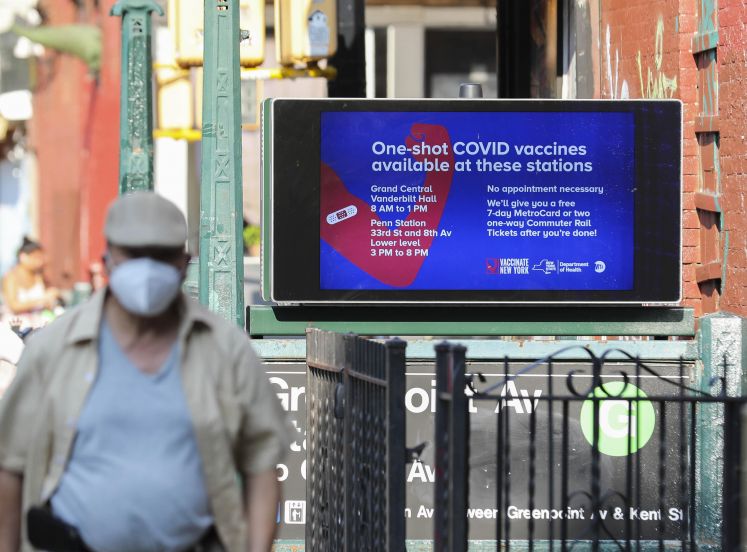 Mann läuft an Werbeplakat für Corona-Impfung vorbei