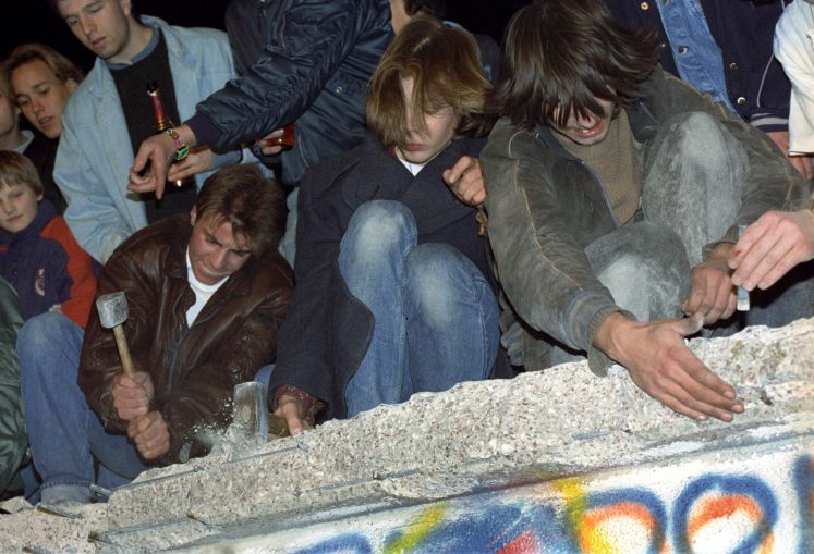 Das Archivbild vom 10.11.1989 zeigt West-Berliner, die mit Hämmern, Kreuzhacken und den bloßen Händen versuchen, die Berliner Mauer einzureißen.