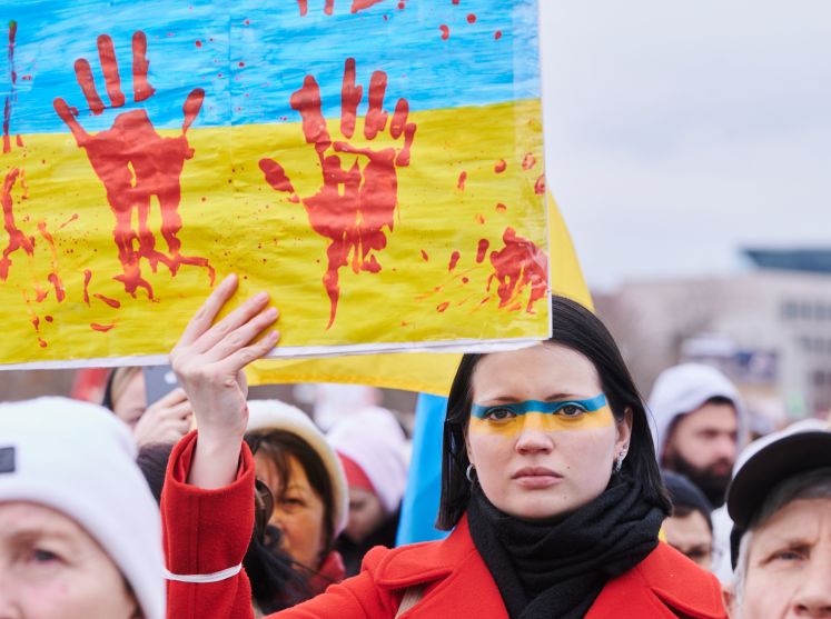 Sophia, geboren in Russland, aber bis vor kurzem in Kiew lebend, hält ein Schild auf dem rote Handabdrücke zu sehen sind. Sie protestiert zusammen mit vielen weiteren Demonstrantinnen und Demonstranten auf der Wiese vor dem Reichstagsgebäude.