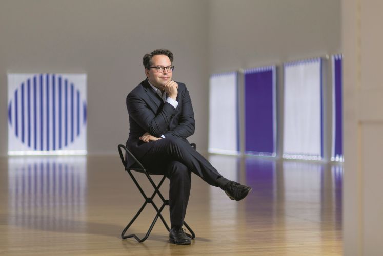  Der Kunsthistoriker Frédéric Bußmann sitzt mit gekreuzten Beinen auf einem Stuhl