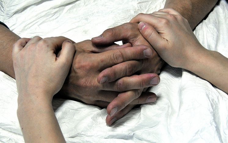 junge Hände umfassen ältere auf einem weißen Bettlaken 