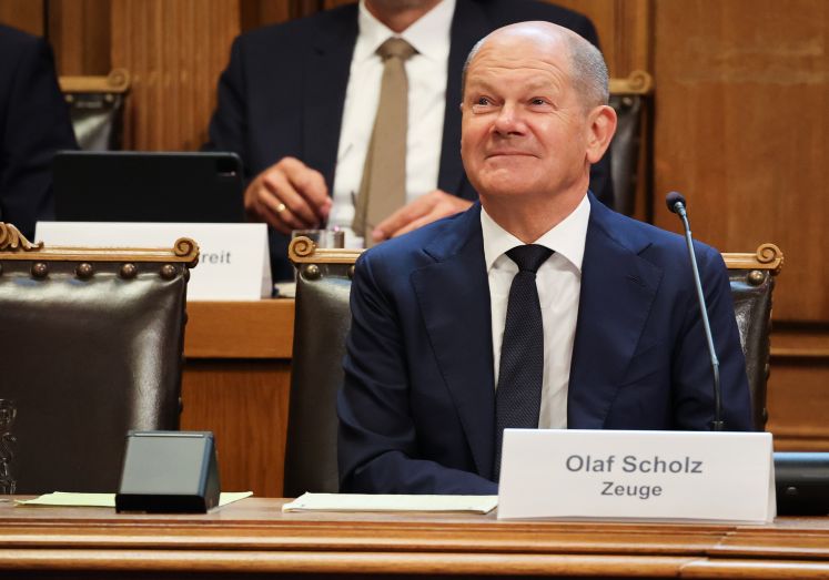 Bundeskanzler Olaf Scholz (SPD) sitzt auf seinem Platz auf der Senatsbank mit einem Plastikschild mit dem Text „Olaf Scholz Zeuge“ vor Beginn einer Sitzung des Parlamentarischen Untersuchungsausschusses „Cum-Ex“ im Plenarsaal der Hamburgischen Bürgerschaft im Rathaus.