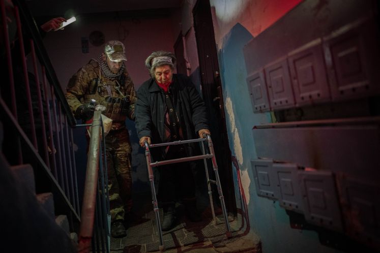 Ein ukrainischer Soldat evakuiert eine alte Frau mit Rollator
