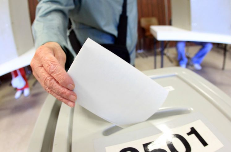 Wähler steckt Stimmzettel in Urne