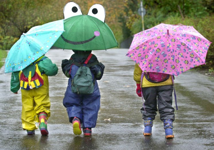 Drei Kinder laufen nebeneinander. Jeder hat einen eigenen Regenschirm.