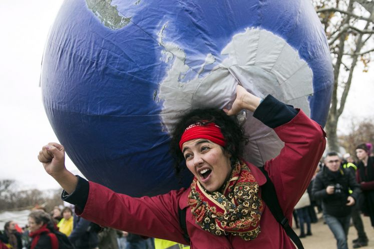 Eine Frau trägt einen aufblasbaren Globus auf ihrem Rücken, während Tausende in Paris für ein Klimaabkommen demonstrieren