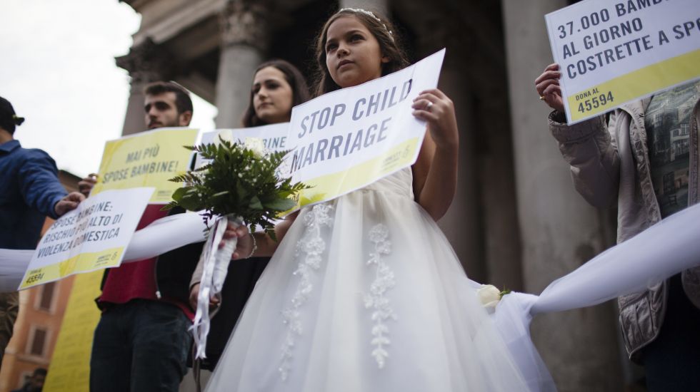 Ein Mädchen hält bei einer Protestaktion im Brautkleid dein Schild in der Hand. Die Aufschrift: Stop child marriage