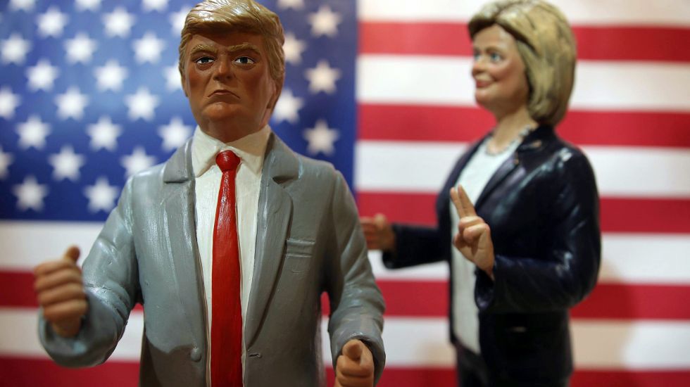 Trump und Clinton als Figuren abgebildet. Er im Vordergrund mit geballten Fäusten, sie im Hintergrund mit der Victory-Geste.