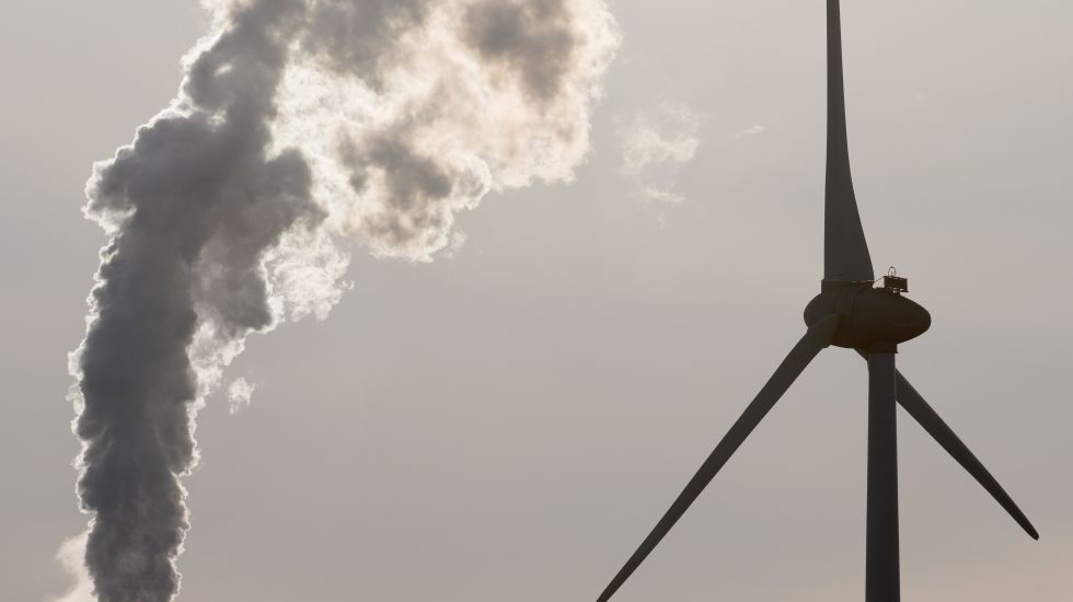 Der rauchende Schlot eines Kohlekraftwerks neben einem Windrad