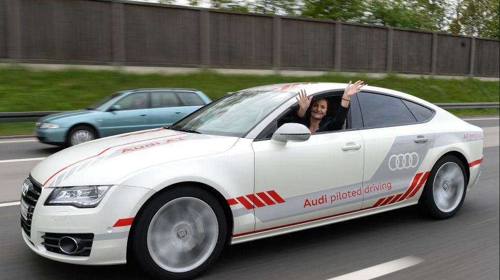 Eine Audi-Mitarbeiterin sitzt während einer Testfahrt auf dem Fahrersitz eines Audi, der über einen Testabschnitt auf der Autobahn A9 bei Ingolstadt fährt und winkt mit beiden Händen aus dem Fenster. 