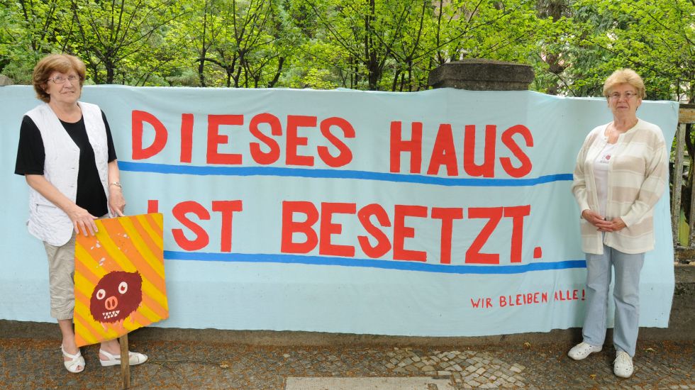 Die Rentnerinnen Brigitte Gall (r) und Ursula Pinotek stehen vor dem besetzten Seniorenklub in Berlin-Pankow, zwischen ihnen hängt ein Banner mit der Aufschrift "Dieses Haus ist besetzt. Wir bleiben alle!".