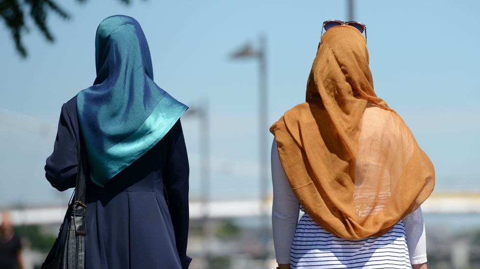 Zwei Frauen mit Kopftuch spazieren in der Sonne.