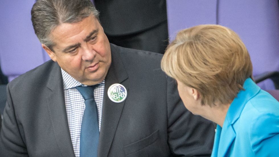 Sigmar Gabriel, den "Wir helfen"-Button am Revers, spricht mit Angela Merkel