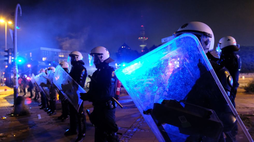 Polizisten stehen mit Schild und Schlagstöcken in einer Reihe und sichern während des G20-Protest eine Straße