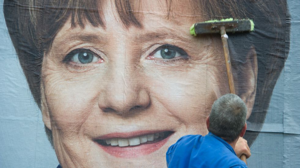 Ein Mann klebt am 09.05.2014 in Stralsund (Mecklenburg-Vorpommern) ein Wahlplakat zum Europawahlkampf mit Bundeskanzlerin Angela Merkel (CDU) auf eine Stellwand