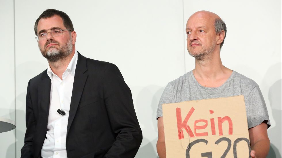 Ein Teilnehmer (r) einer Infoveranstaltung zum G20-Gipfel in Hamburg (07.-08.07.2017) sowie OSZE-Gipfel (08.-09.12.2016) protestiert am 01.09.2016 in Hamburg auf dem Podium mit einem Pappschild mit der Aufschrift «Kein G20». Neben ihm steht der Staatsrat der Senatskanzlei, Wolfgang Schmidt (l).