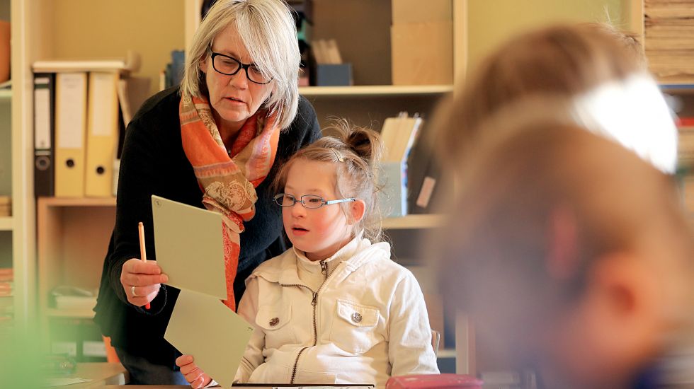 Eine Lehrerin betreut in einer Gemeinschaftsschule ein Mädchen mit Down-Syndrom
