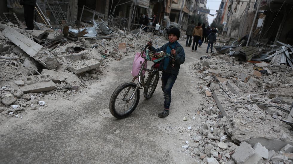 Ein kleiner Junge schiebt umgeben von Trümmern und Häuserskeltten sein Fahrrad.