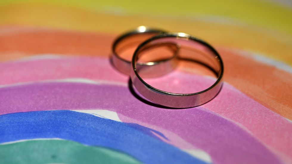 Zwei Eheringe liegen auf einem Bild von einem Regenbogen