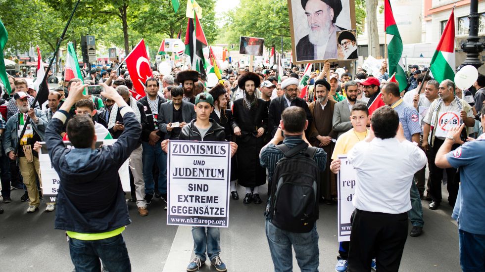 Teilnehmer einer Pro-Palästina-Demo marschieren am 11.07.2015 anlässlich des Al-Kuds-Tag in Berlin. Ein Junge hält dabei ein Schild mit der Aufschrift "Zionismus und Judentum sind extreme Gegensätze". Andere Teilnehmer halten ein Bild von Ajatollah Khomeini hoch.
